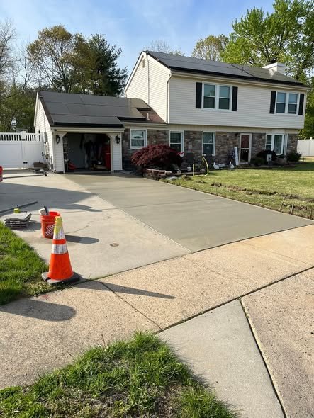 New concrete driveway beside a two-story home with a safety cone set out while the fresh slab cures