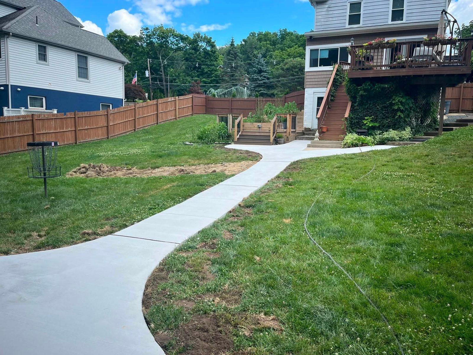 Long curving backyard concrete walkway through a lawn toward a deck
