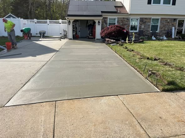 Freshly poured single-car concrete driveway lane with a broom finish and tooled control joints